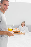 Smiling man bringing breakfast in bed to his partner