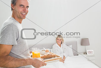 Cheerful man bringing breakfast in bed to his partner