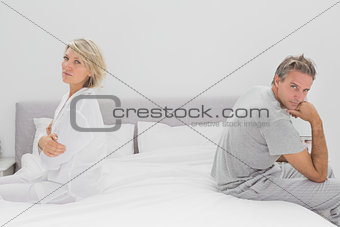 Couple sitting on opposite sides of bed looking at camera