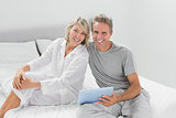 Couple using their digital tablet smiling at camera