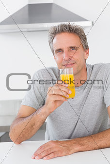 Cheerful man having glass of orange juice in kitchen