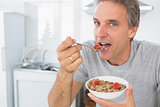 Happy man eating cereal for breakfast in kitchen