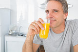 Happy man drinking orange juice in kitchen