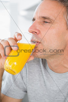 Content man drinking orange juice in kitchen