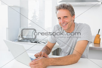 Cheerful man using laptop in kitchen