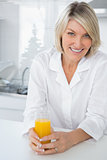 Cheerful blonde having orange juice in kitchen