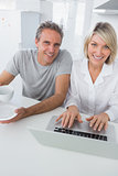 Cheerful couple using laptop in the morning looking at camera