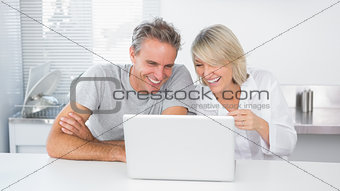 Happy couple laughing at laptop in the morning