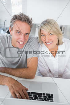 Smiling couple using their laptop in the morning looking at camera