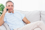 Man on his couch making phone call and smiling at camera