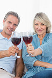 Couple toasting to the camera with red wine on the couch