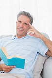Man relaxing on his couch with a book smiling at camera