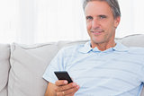 Man relaxing on his couch sending a text smiling at camera