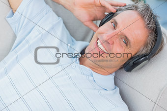 Man lying on sofa listening to music smiling at camera
