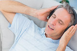 Man lying on sofa listening to music with eyes closed