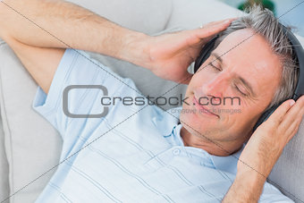 Man lying on couch listening to music with eyes closed