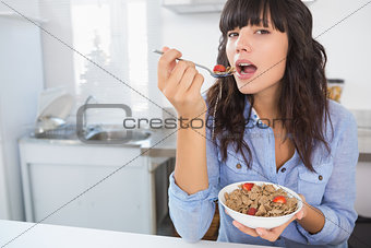 Cheerful brunette eating bowl of cereal and fruit