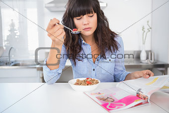 Pretty brunette having cereal and reading magazine