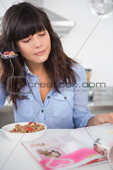 Pretty brunette eating cereal and reading magazine