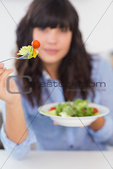 Pretty brunette showing her fork of salad to camera