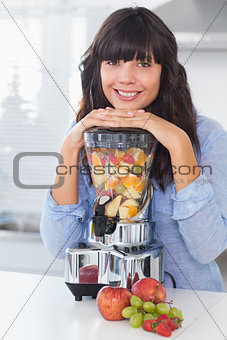 Smiling brunette leaning on her juicer full of fruit