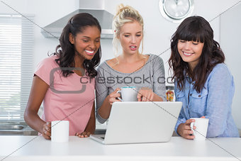 Happy friends having coffee together and looking at laptop
