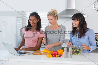 Smiling friends making salad and using laptop for recipe