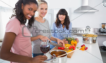 Smiling friends preparing a meal together looking at camera