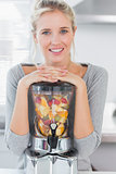 Blonde woman leaning on her juicer full of fruit and smiling at camera