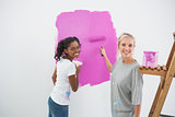 Smiling young housemates painting wall pink