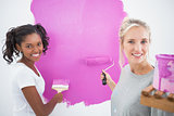 Smiling housemates painting wall pink