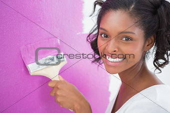 Smiling young woman painting her wall in pink
