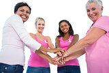Smiling women wearing breast cancer ribbons putting hands together smiling at camera