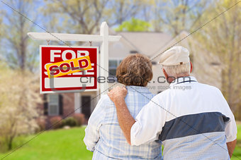 Senior Couple in Front of Sold Real Estate Sign and House