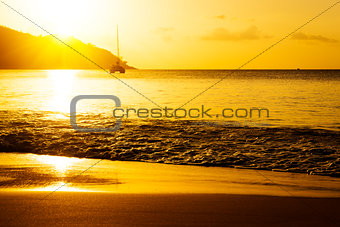 Yacht near rocky coast of seychelles. Gold sunset on sand beach