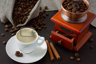 A cup of coffee near roasted coffee beans and a coffee grinder