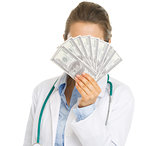 Doctor woman hiding behind fan of dollars