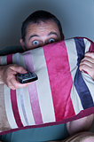man covering face with a cushion watching tv