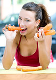 Beautiful young woman eating a carrot in the kitchen