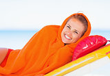 Smiling young woman wrapped in towel laying on sunbed