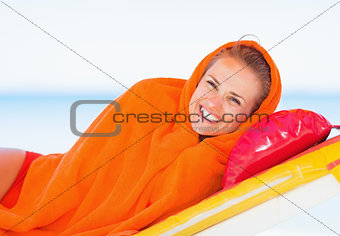 Smiling young woman wrapped in towel laying on sunbed
