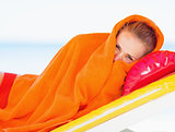 Young woman wrapped in towel laying on chaise-longue