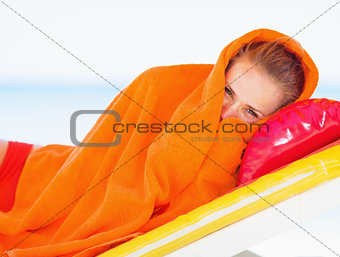 Young woman wrapped in towel laying on chaise-longue