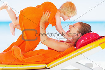 Happy mother and baby playing on chaise-longue