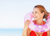 Portrait of smiling young woman on beach with swim ring looking 