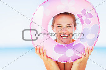 Smiling young woman on beach looking through swim ring