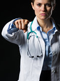 Closeup on doctor woman pointing in camera isolated on black