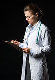 Doctor woman writing in clipboard isolated on black