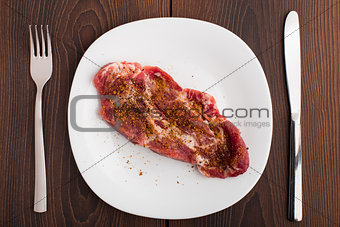 Raw steak with spices on white plate