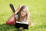 young girl reading book lying on the grass